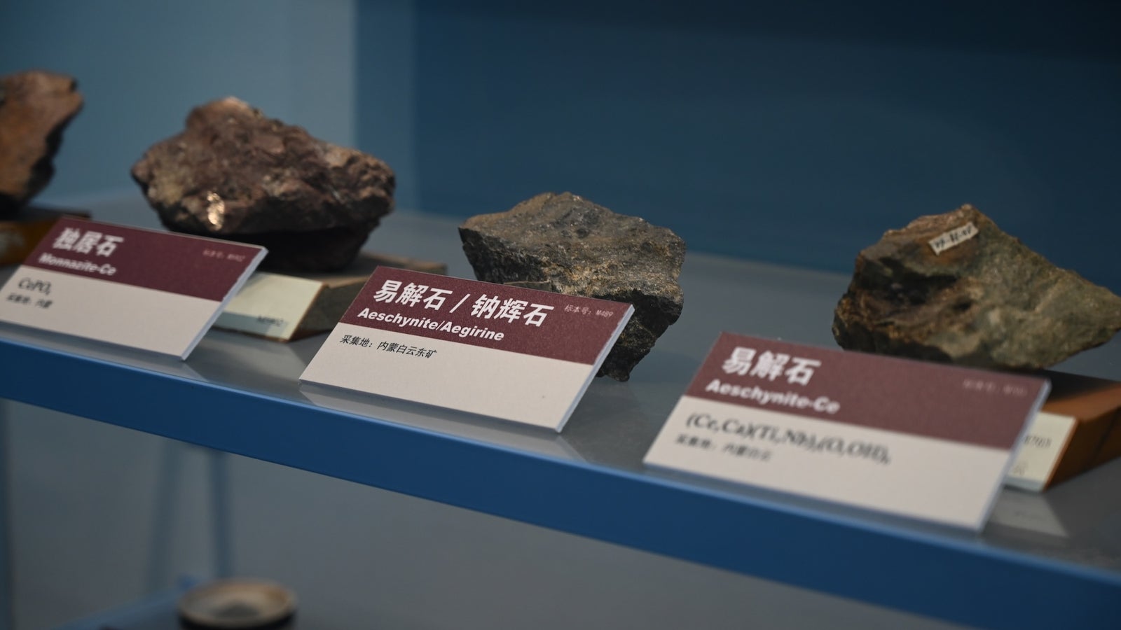 Several types of rocks displayed on shelves with labels, including Aeschynite and Monazite