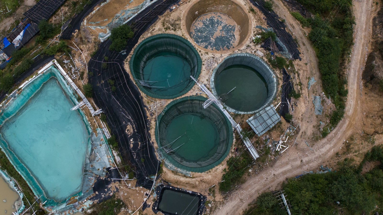 Aerial view of several circular water tanks and shallow ponds surrounded by black tarps and undeveloped land