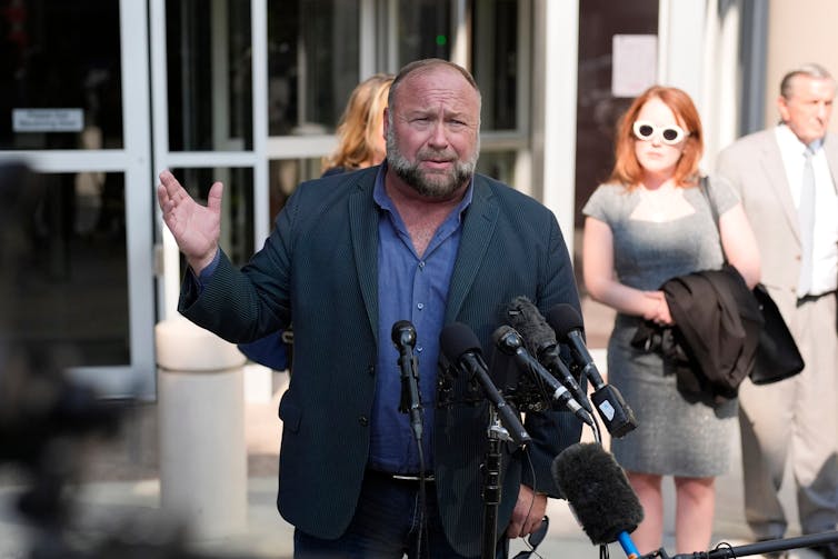 Alex Jones in front of microphones, looking annoyed