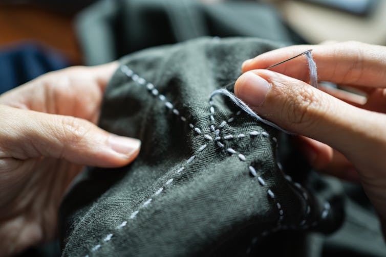 person's hands sewing blue stitches into dark grey fabric