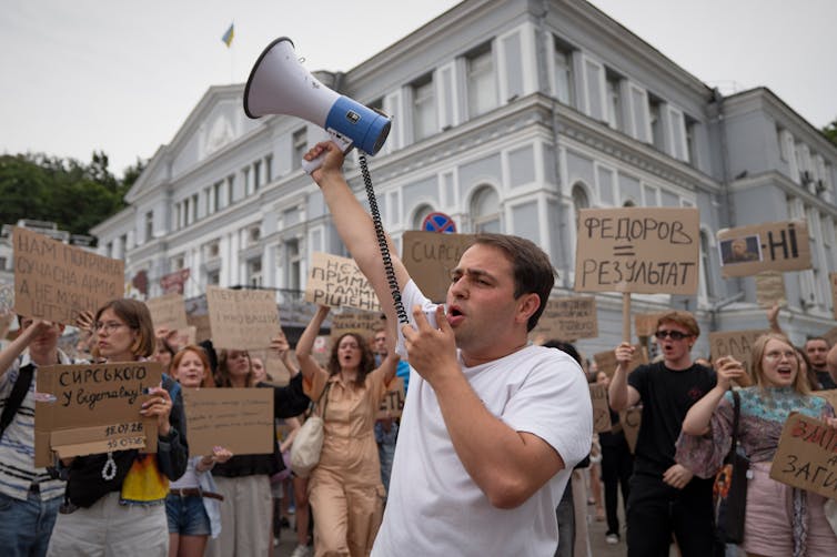 A man in a white T-shirt speaks into a megaphone.