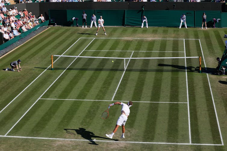 Whole-court view of a player serving at Wimbledon as his opponent prepares to return the serve.