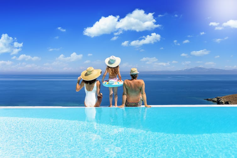 Family sitting on edge of swimming pool looking out to sea.