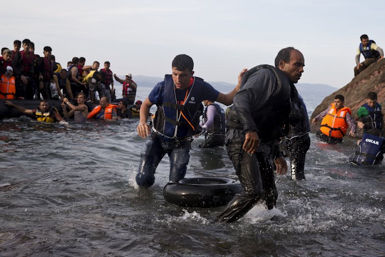 People walk onto a shore from makeshift boats.