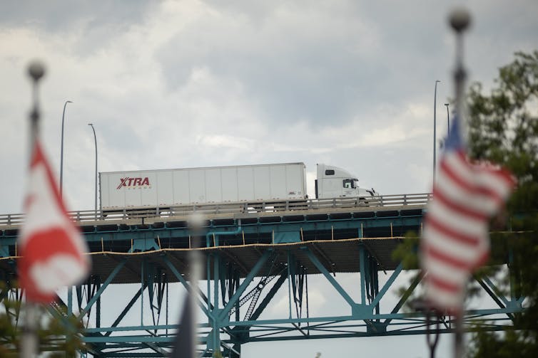 A truck crosses a bridge with a Canadian flag and American flag seen in the foreground