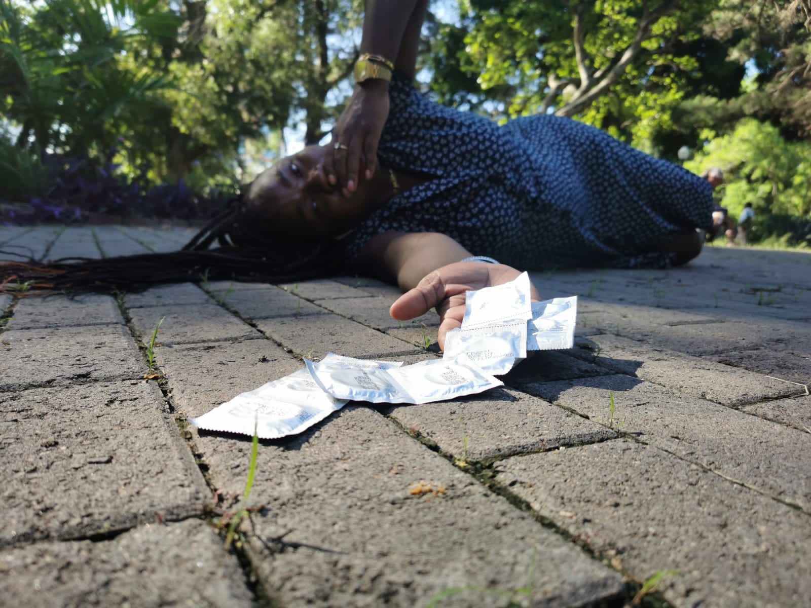 A woman lies on the ground, one hand covering her mouth, the other with several condoms in their packets spilling out of it