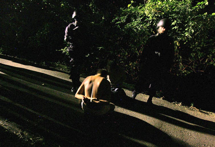 Two men in uniform stand guard over a man in handcuffs.