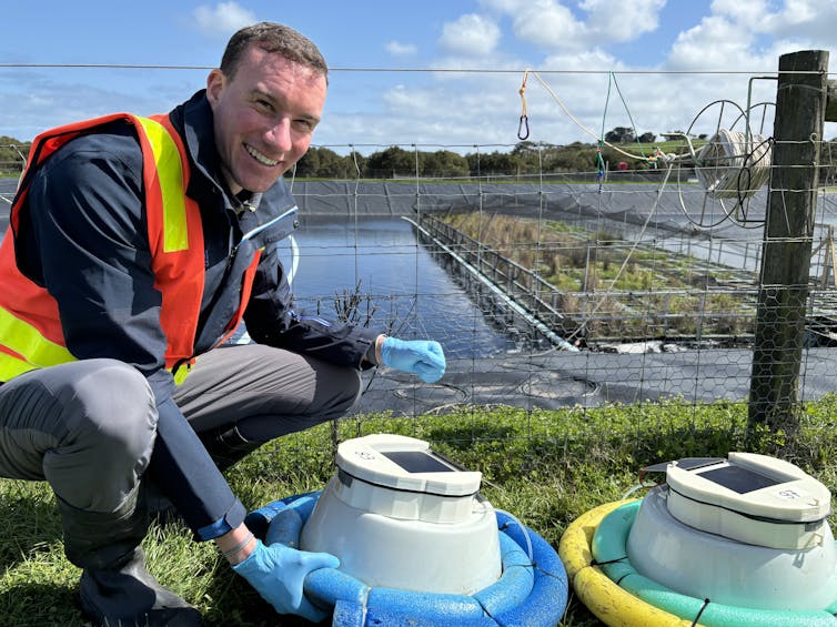A smiling man in a high vis jacket looks at equipment with a wetland in the background.