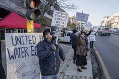 People stand on a road with signs saying 'We stand together for fair water access' and 'United for water equity'