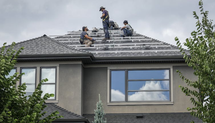 Workers install solar panels on a residential home