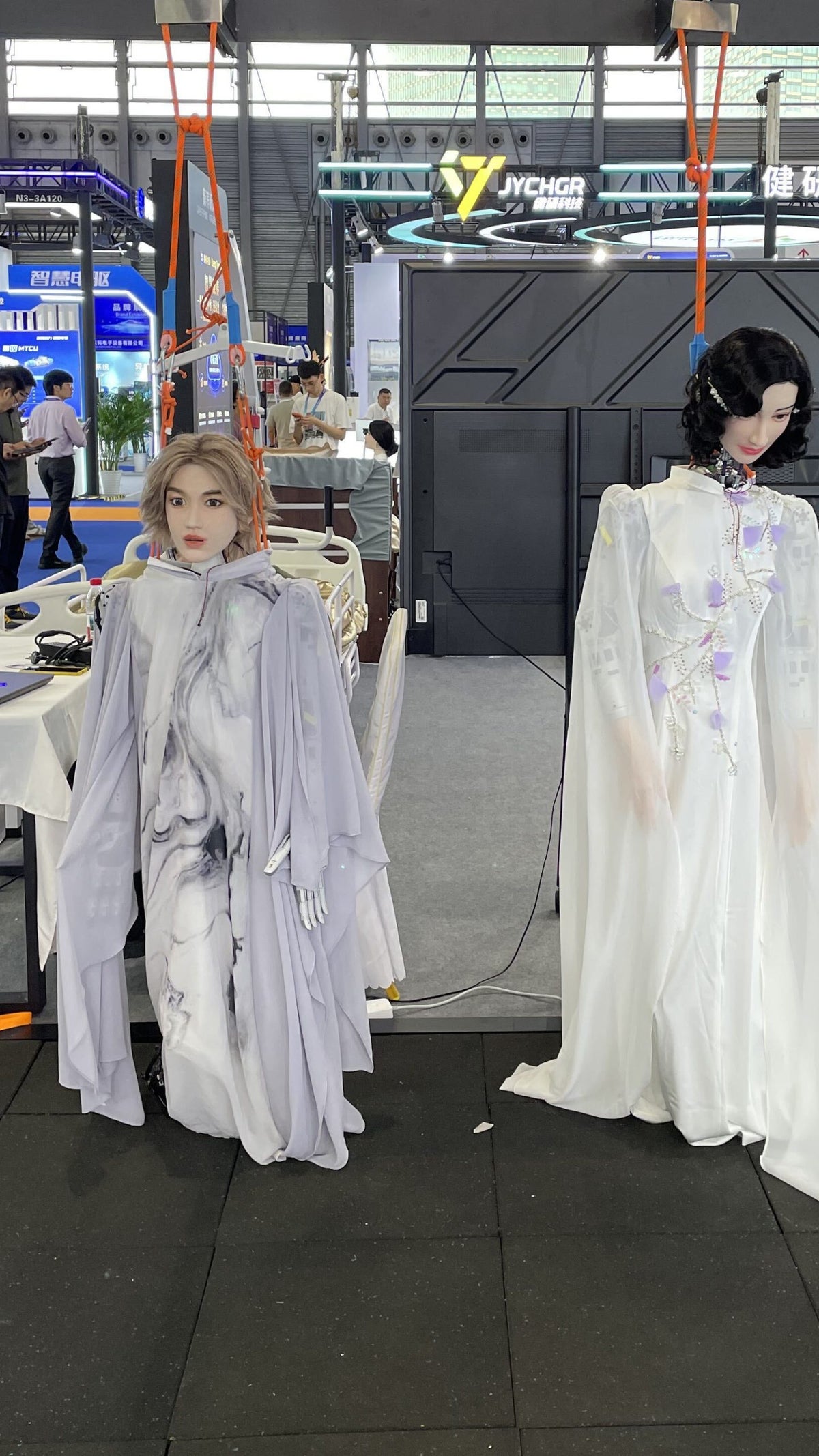 Two mannequins dressed in elegant robes, one gray and the other white, displayed at an exhibition venue