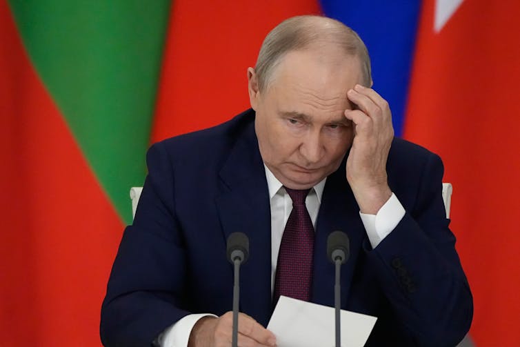 Russian president Vladimir Putin holds his hand to his head.