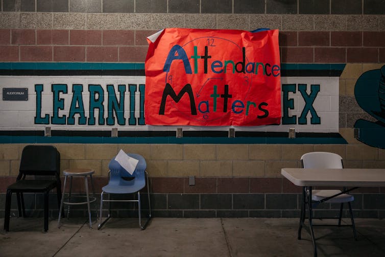 A hand-drawn red sign that says 'Attendance matters' is hung on a tile wall with chairs nearby.