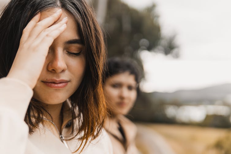 Person turned away from another person, hand pressed to their forehead with closed eyes