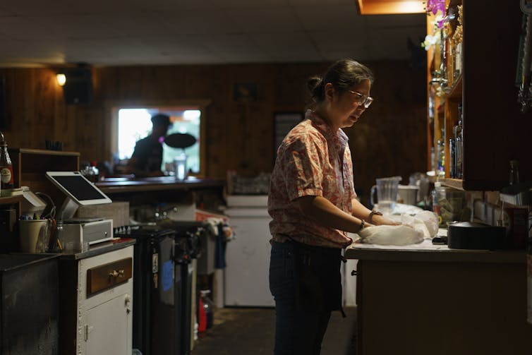 A woman in a small commercial kitchen preps a takeout order.