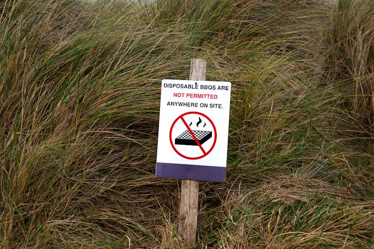 sand dune grass, white signpost says disposable barbecues are not permitted on this site