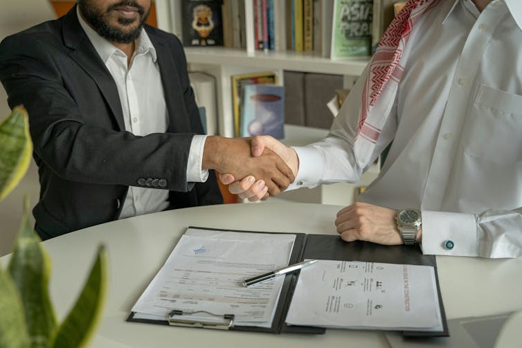 Two men shaking hands over signed documents