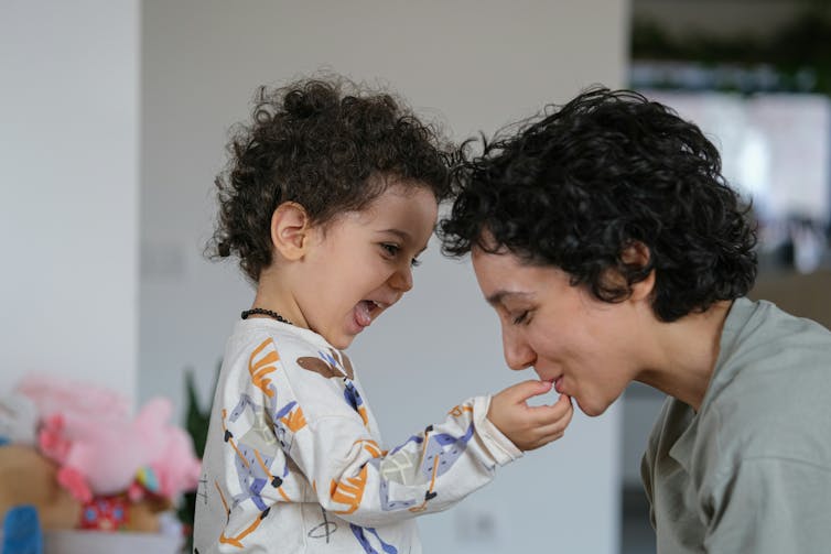 A mother seen playfully kissing her child's hand and the child is laughing.
