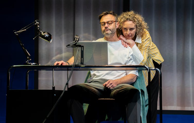 Production image: a man at a laptop, a woman leans on his shoulders.
