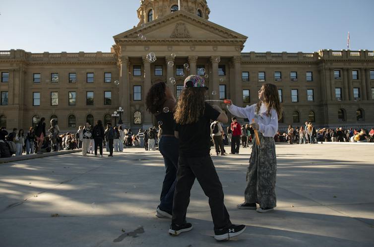Students stand in front of a stone legislative building blowing bubbles.