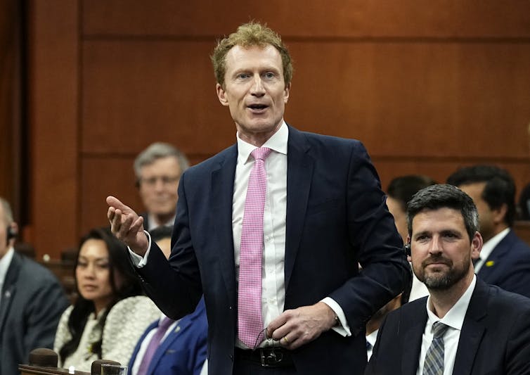 a man stands surrounded by several seated people