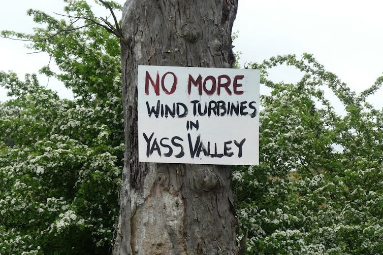 sign saying no more wind turbines nailed to a tree.