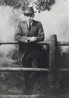 A man in a hat leaning on a wooden fence.