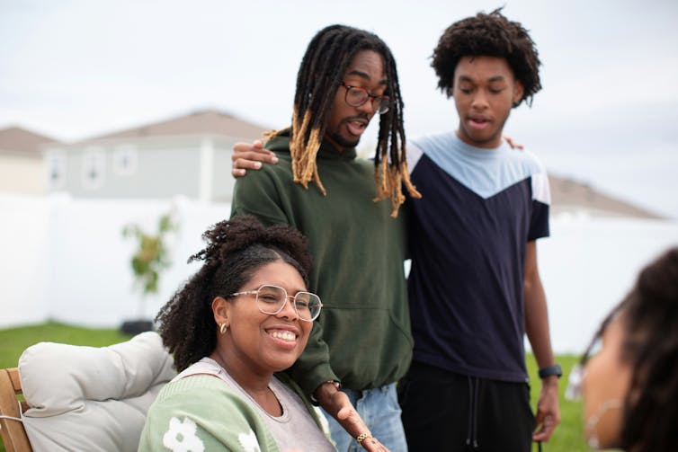 Some young men listen in on a discussion of a woman who is seated in discussion.