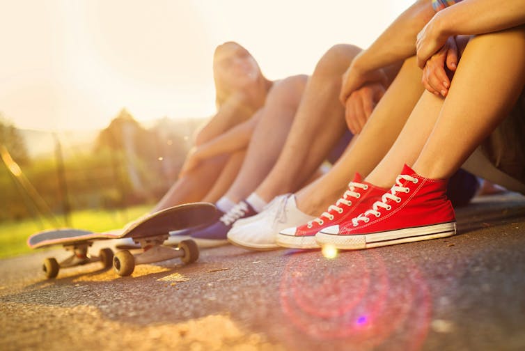 A row of teens' feet seen with a skateboard.