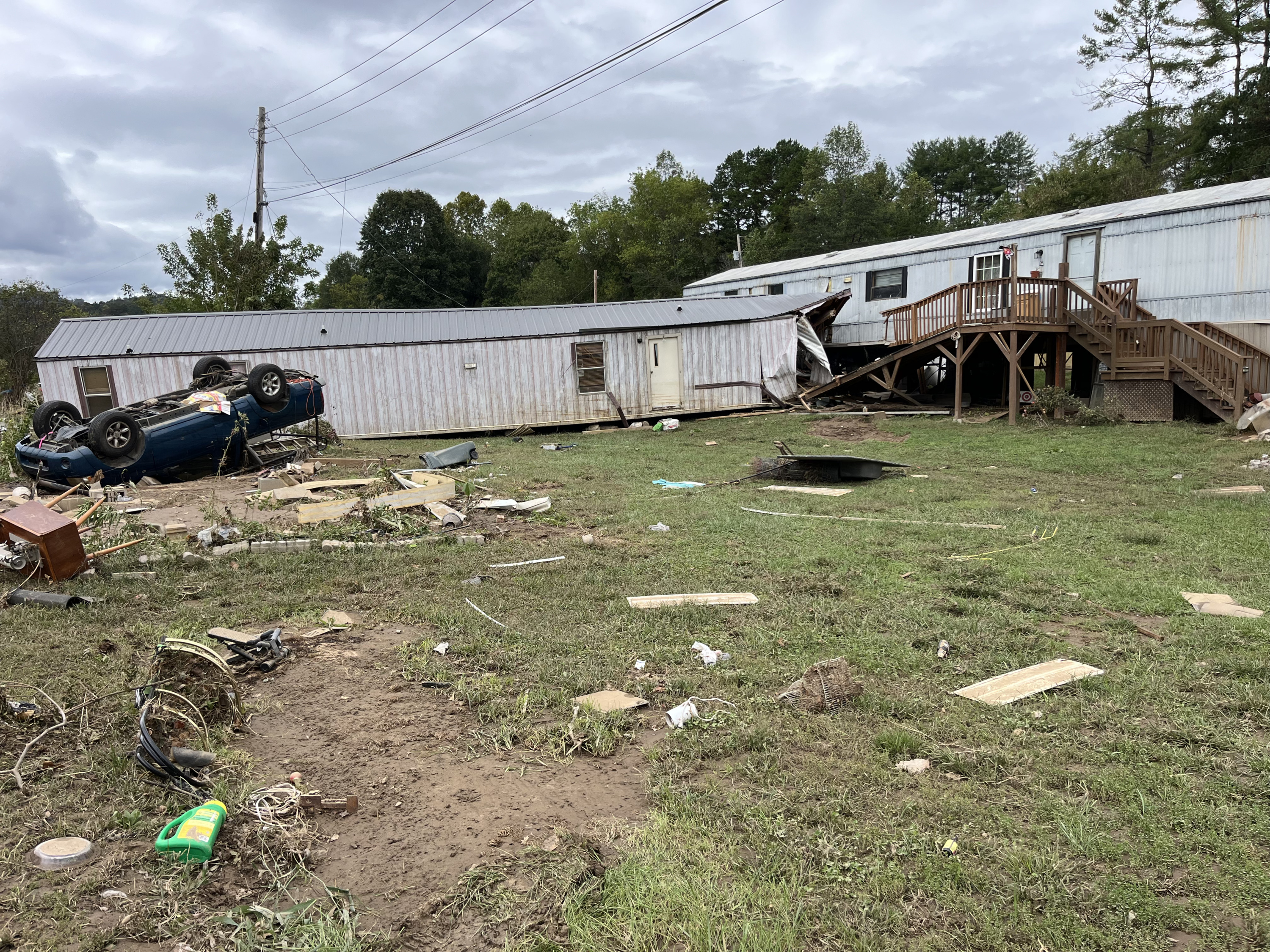 Debris litters a lawn where a car lies on its roof and two trailer homes have crashed into each other.