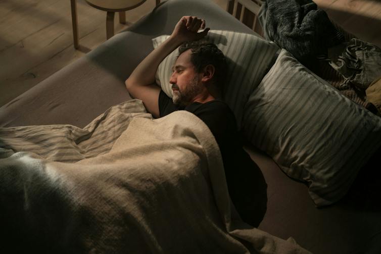 A man lies in bed in a dark room