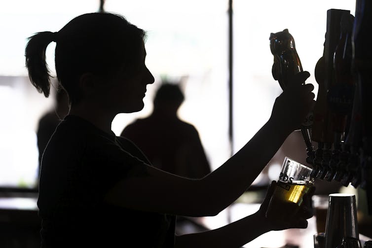 Silhouette of a bartender filling a glass with beer from a tap
