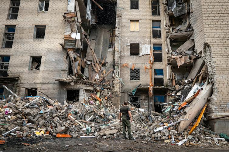 A tall residential apartment building partially damaged with a chunk missing from the middle and a large pile of debris at the bottom