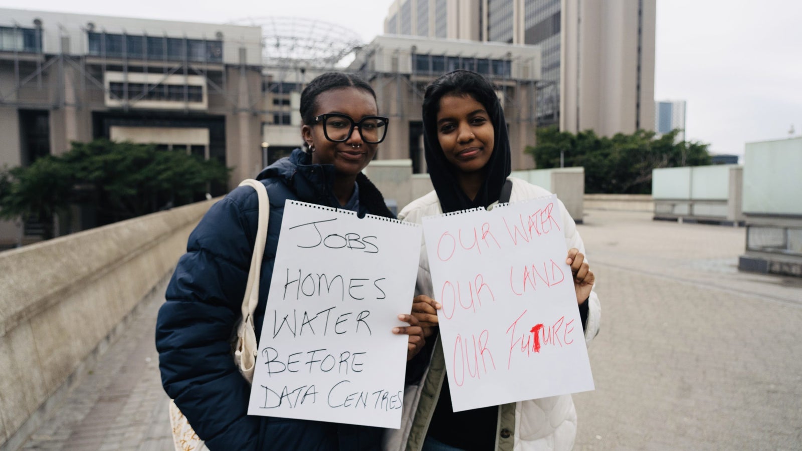 Two young women hold signs protesting for priorities such as jobs, homes, and water over data centers