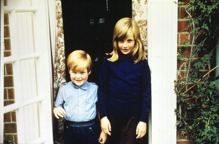A small boy with his older sister, outside a house.