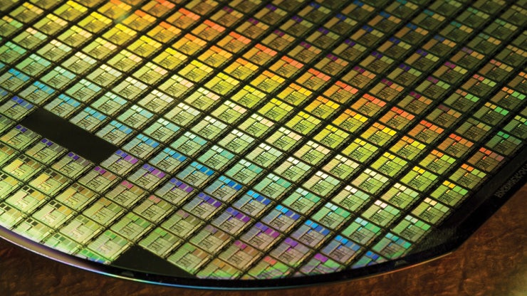 A close-up view of a shiny silicon wafer filled with intricately patterned microchips arranged in a grid