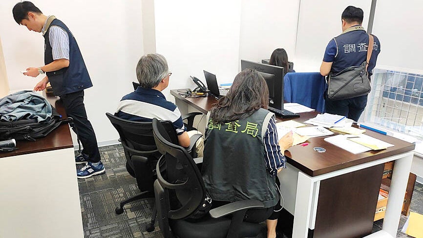 A group of people in an office setting, some seated at desks with computers, and others standing, all wearing uniforms