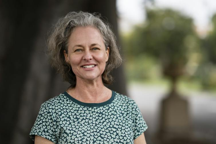 A grey-haired woman smiling outside, wearing a patterned green t-shirt.