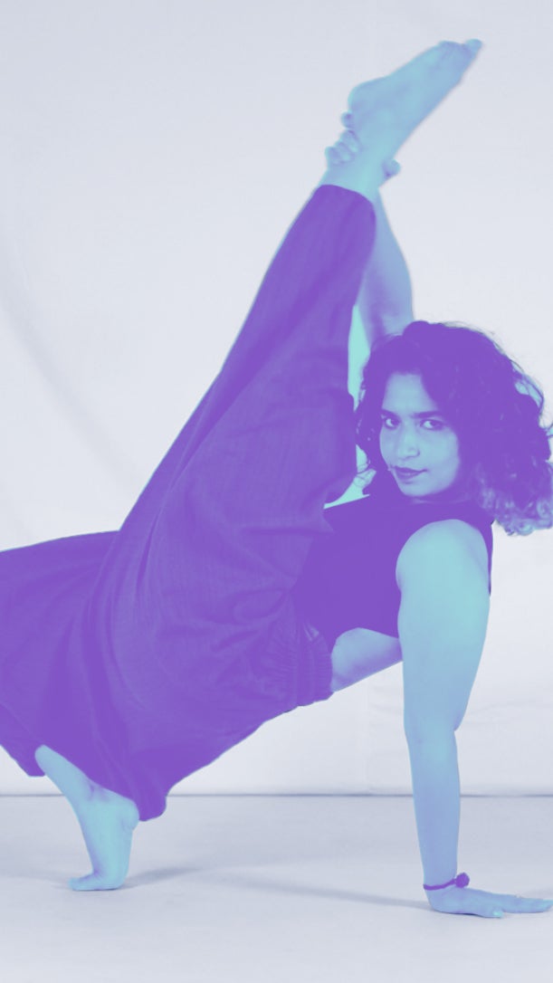A person performs a dance pose on one hand, with one leg raised high, against a soft background