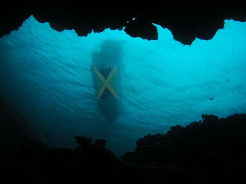 Feature image of an underwater shot of a vessel with a Jamaican flag on its hull, created by Janine Mendes-Franco using Canva Pro elements. 
