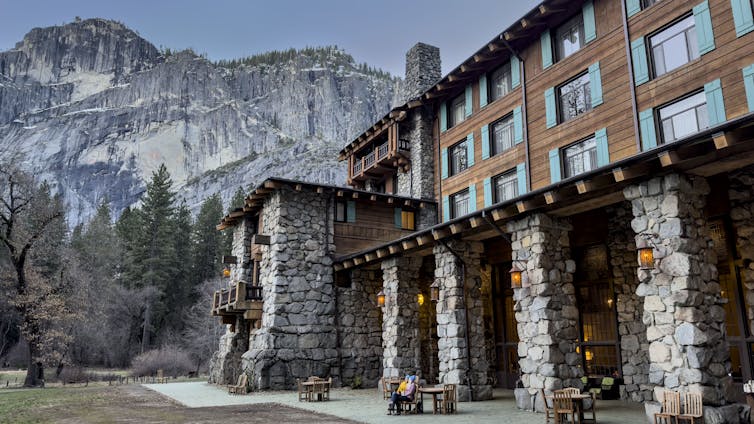 A large building stands in front of a massive set of cliffs.