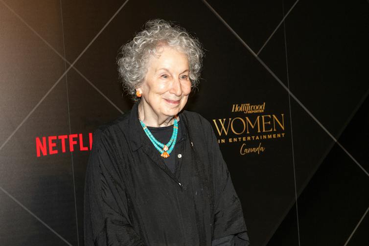 A woman in a dark dress stands in front of a backdrop that says Hollywood and Netflix.