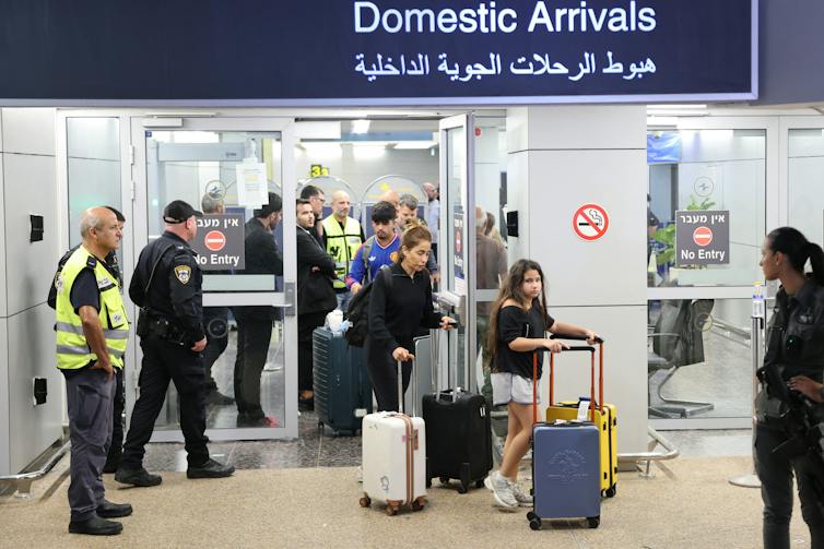 Passengers pushing luggage walk under a sign that says 'Domestic Arrivals'