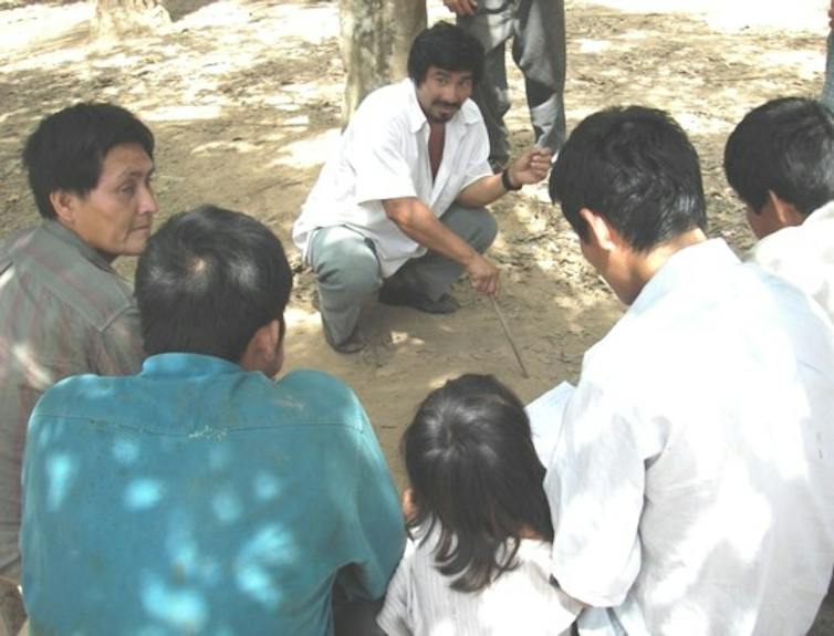semi circle of people outside facing a man squatting on the ground