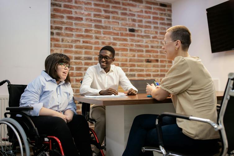 A small group having a conversation in a meeting or shared workspace. One person is in a wheelchair