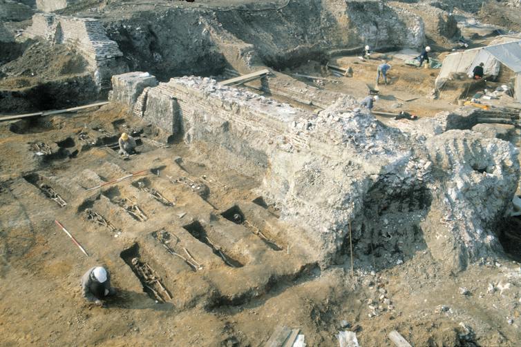 An excavation, showing skeletons in graves.