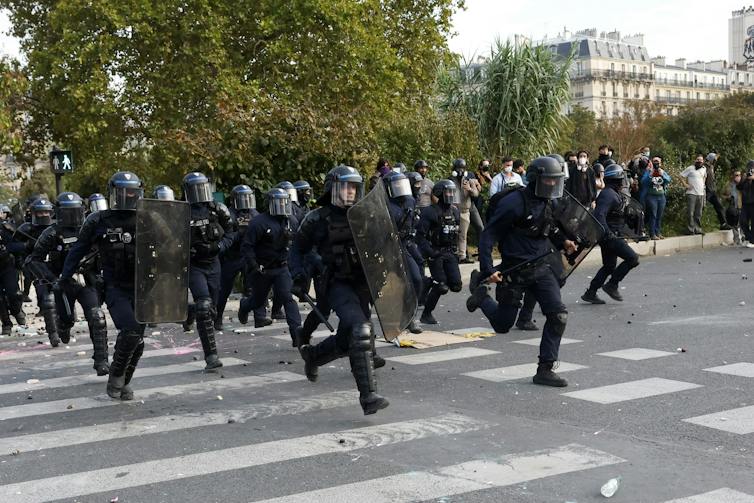 French police in riot gear run across a road in Paris.