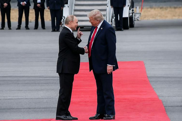 US president Donald Trump and Russian president Vladimir Putin stand togather on a red carpet in Alaska.
