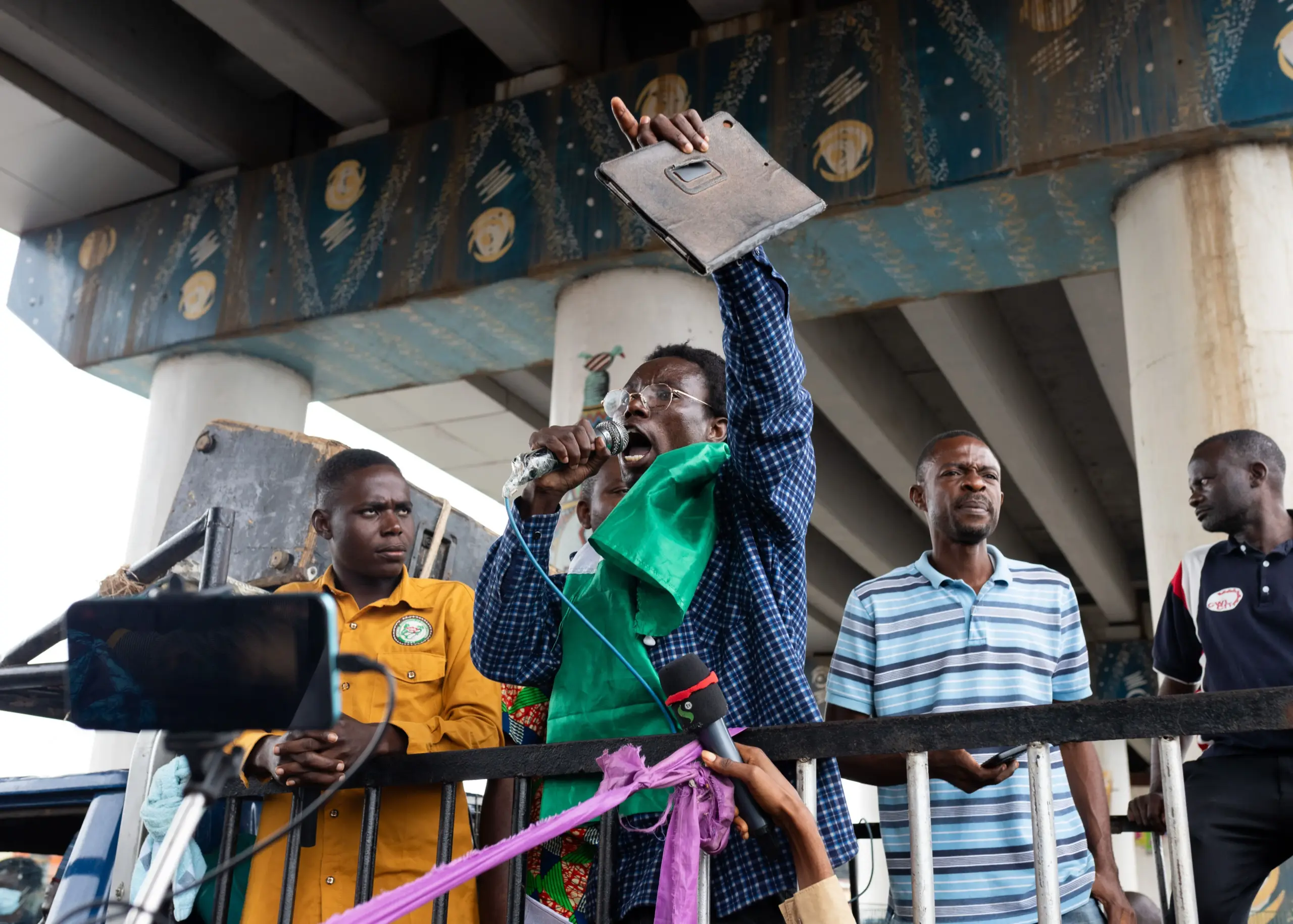 A group of men during a peaceful protest; one of them holds a microphone and a banner.