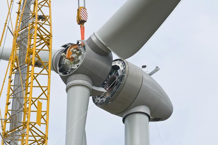 wind turbine being erected, blades being installed on base using a crane.